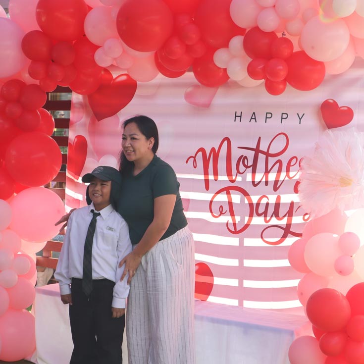 Good Shepherd Primary Plumpton Mother and Son standing in front of balloons and a banner which reads Happy Mother's Day